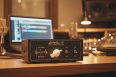 A professional 16-24 channel portable analog summing mixer on a desktop studio workstation featuring premium control knobs and VU meters.